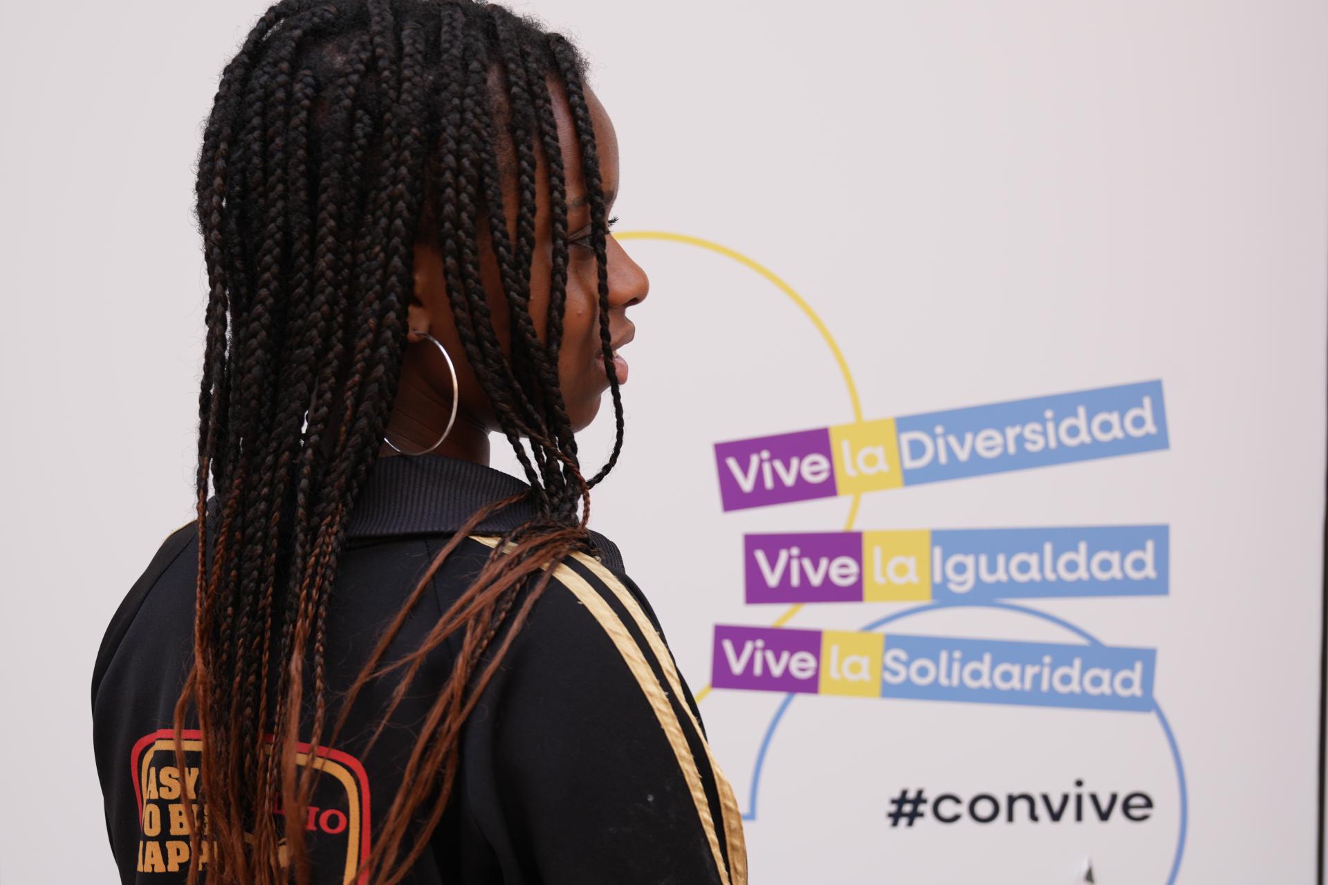 imagen de niña negra de espaldas al fondo un letrero en colores azul, amarillo y magenta vive la igualdad, vive la diversidad, viva la solidaridad, convive